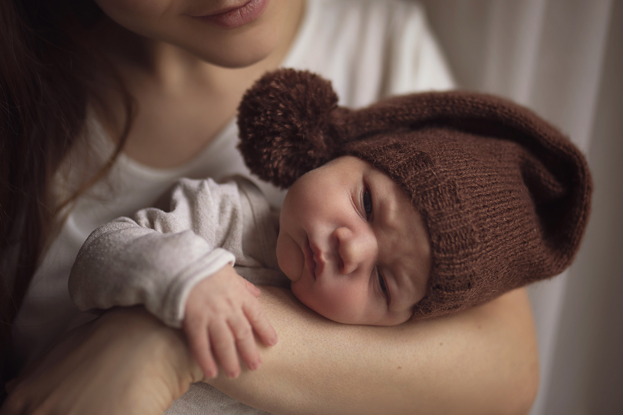 Mother holding an infant in a brown knit cap