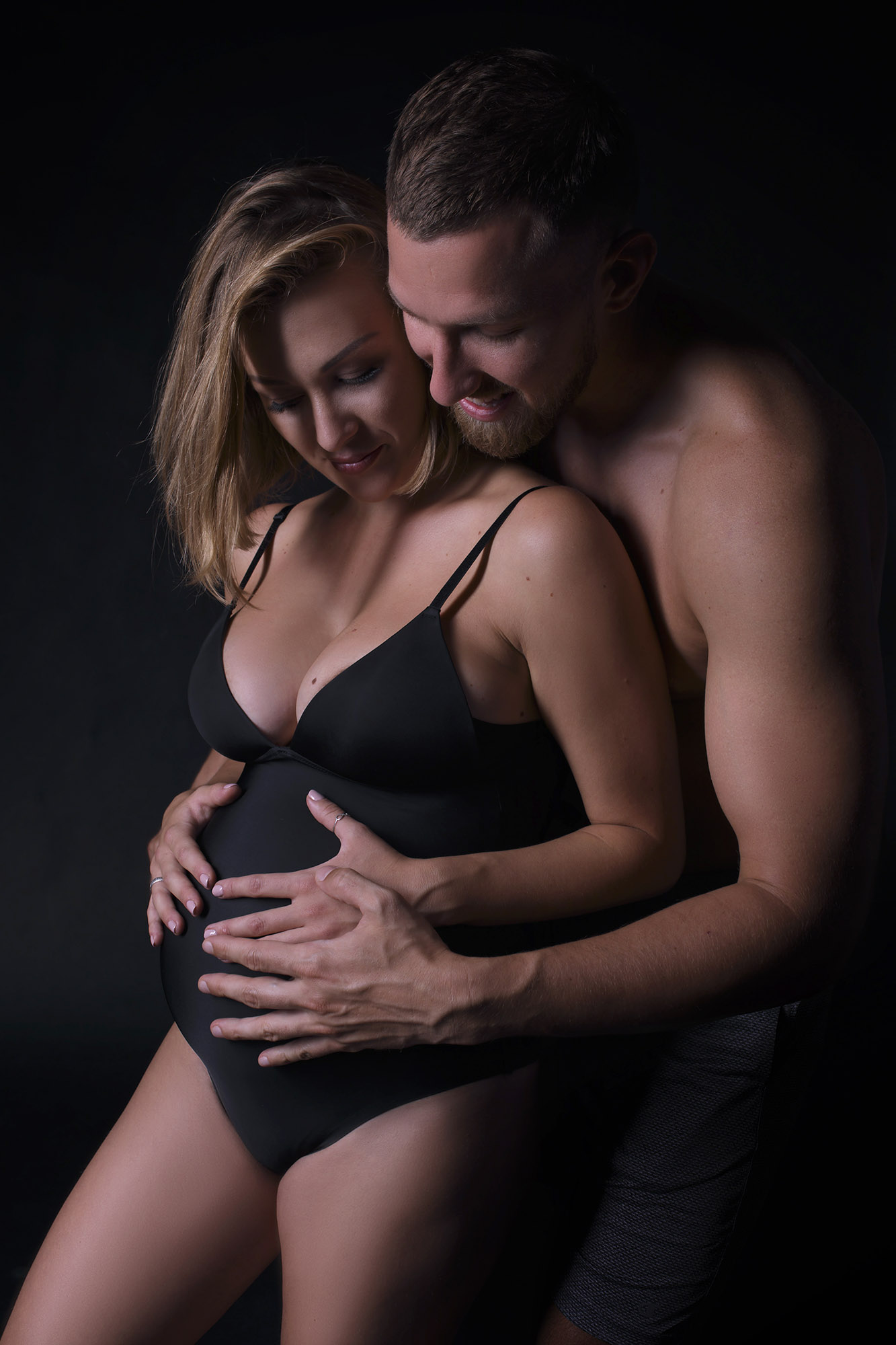 Man is hugging a pregnant woman in black lanerie
