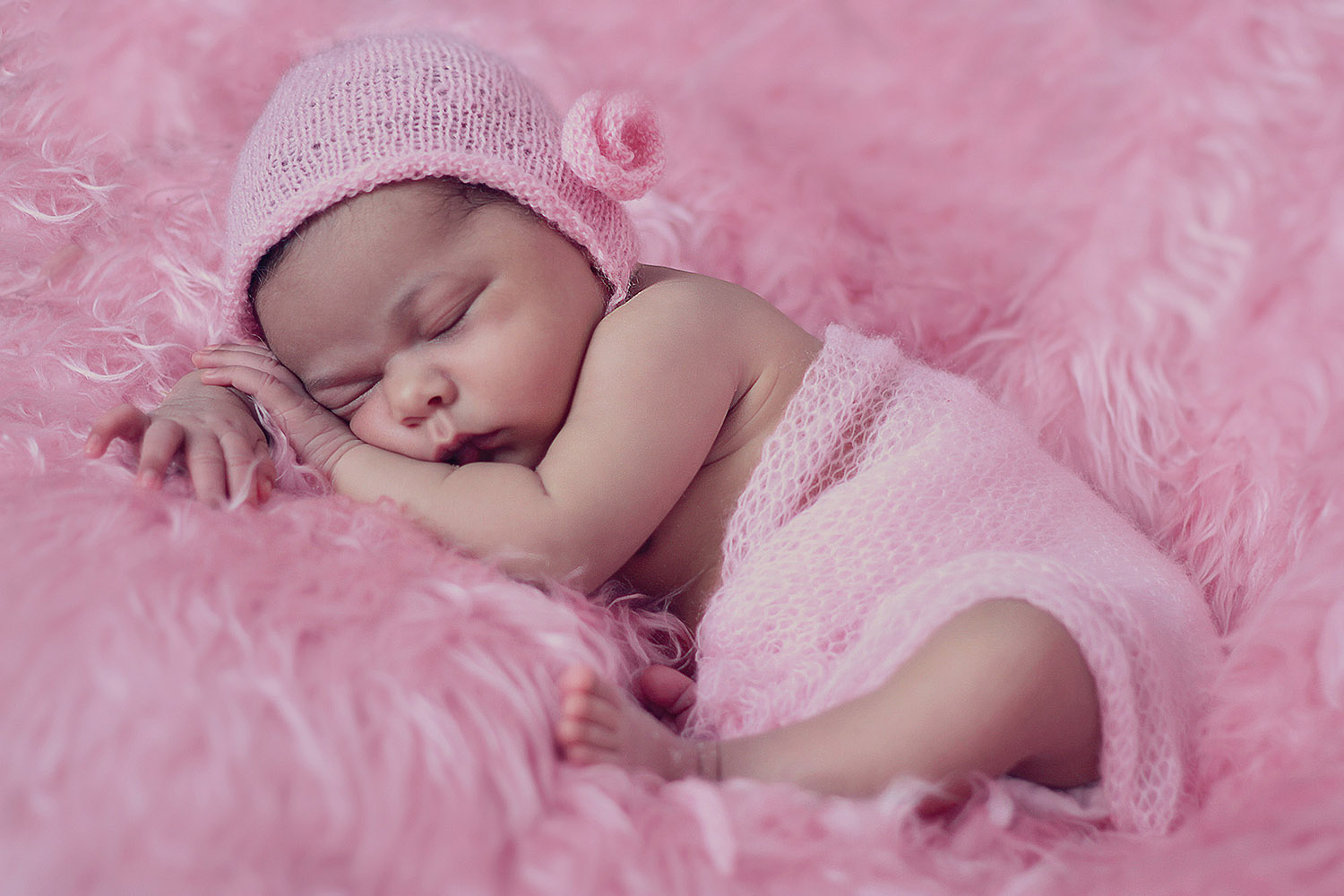 Sleeping infant in knit cap on a pink fur