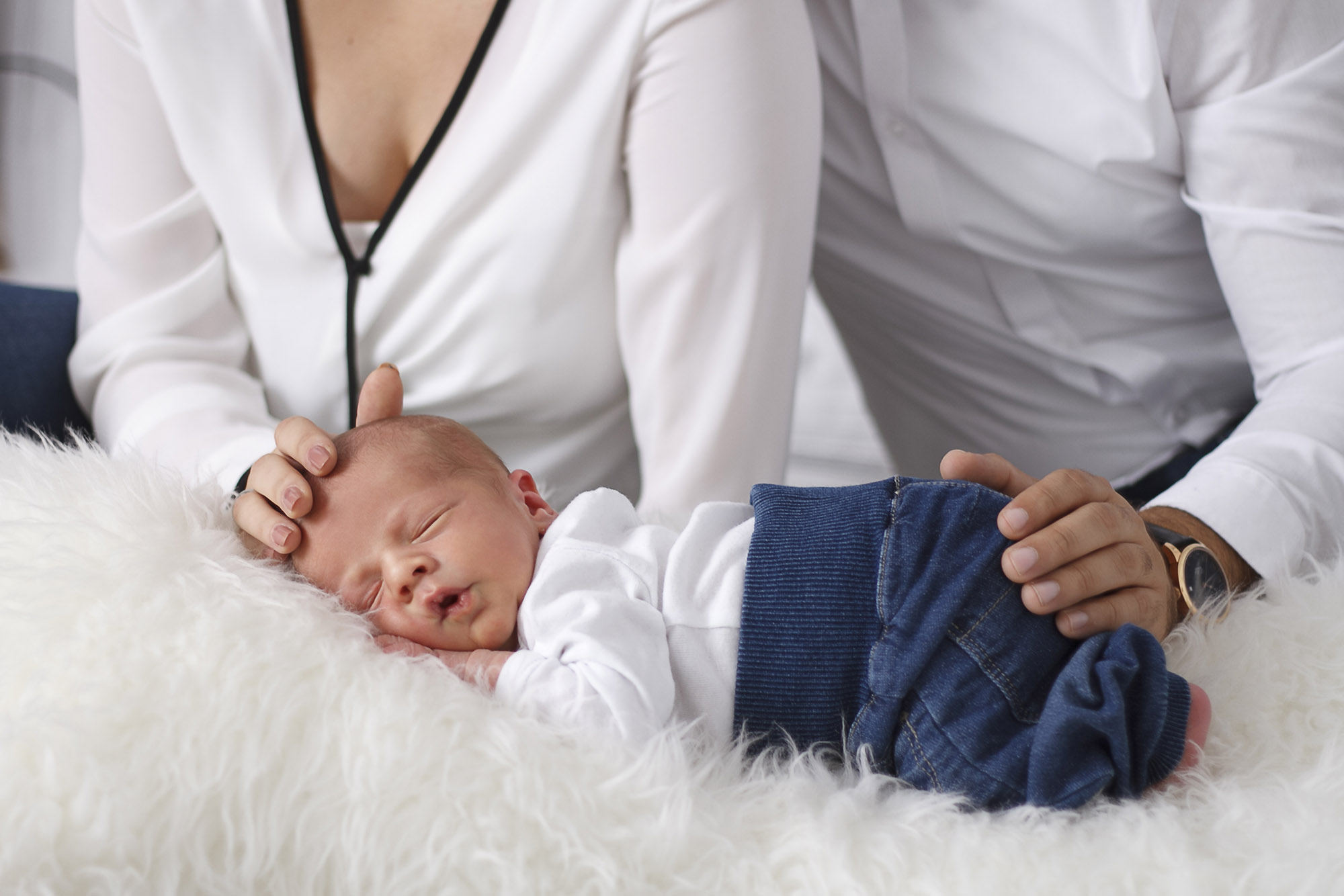 Sleeping infant on fur with his mother and father on the background