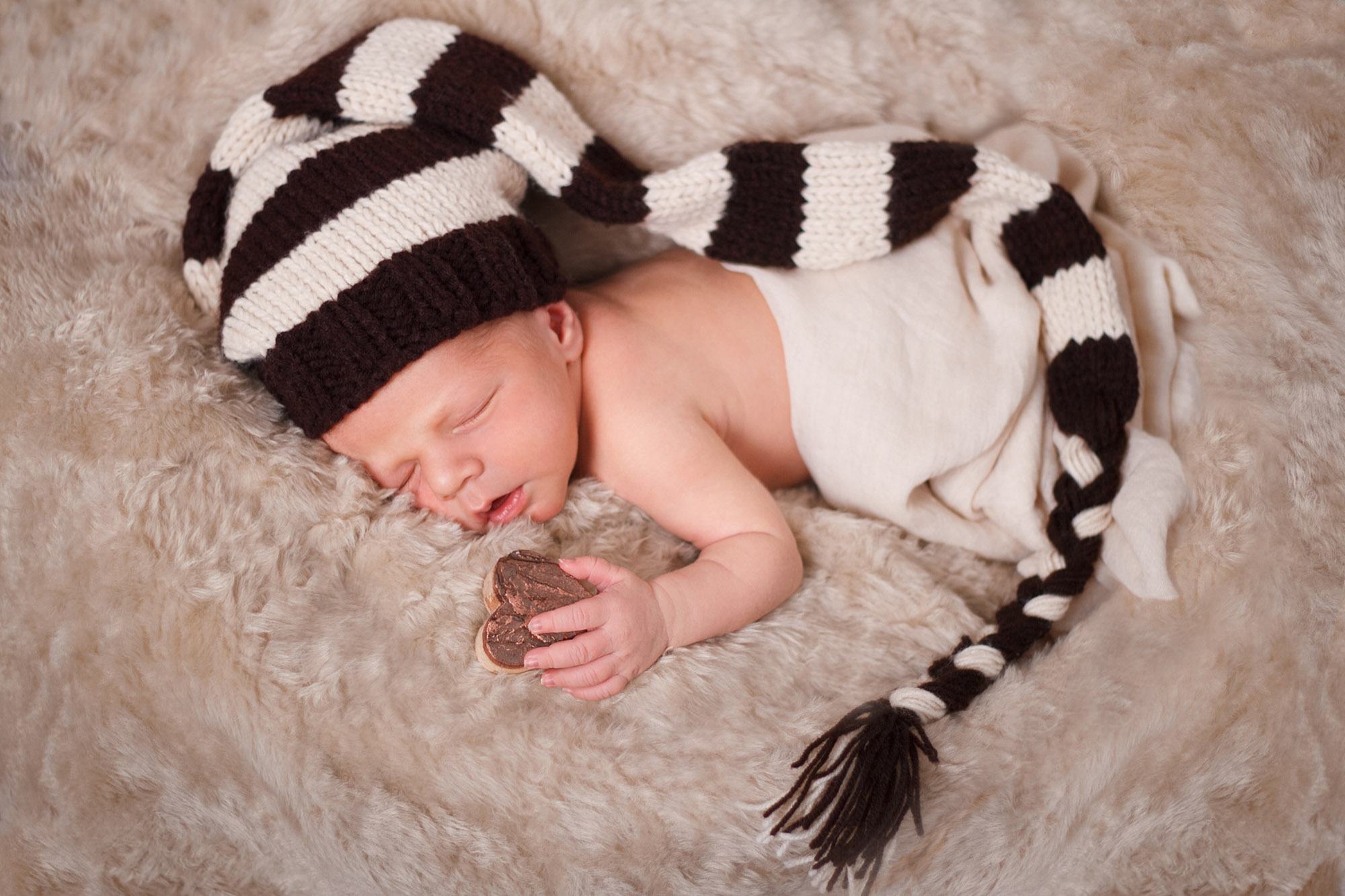 Sleeping infant holding a cookie on a fur