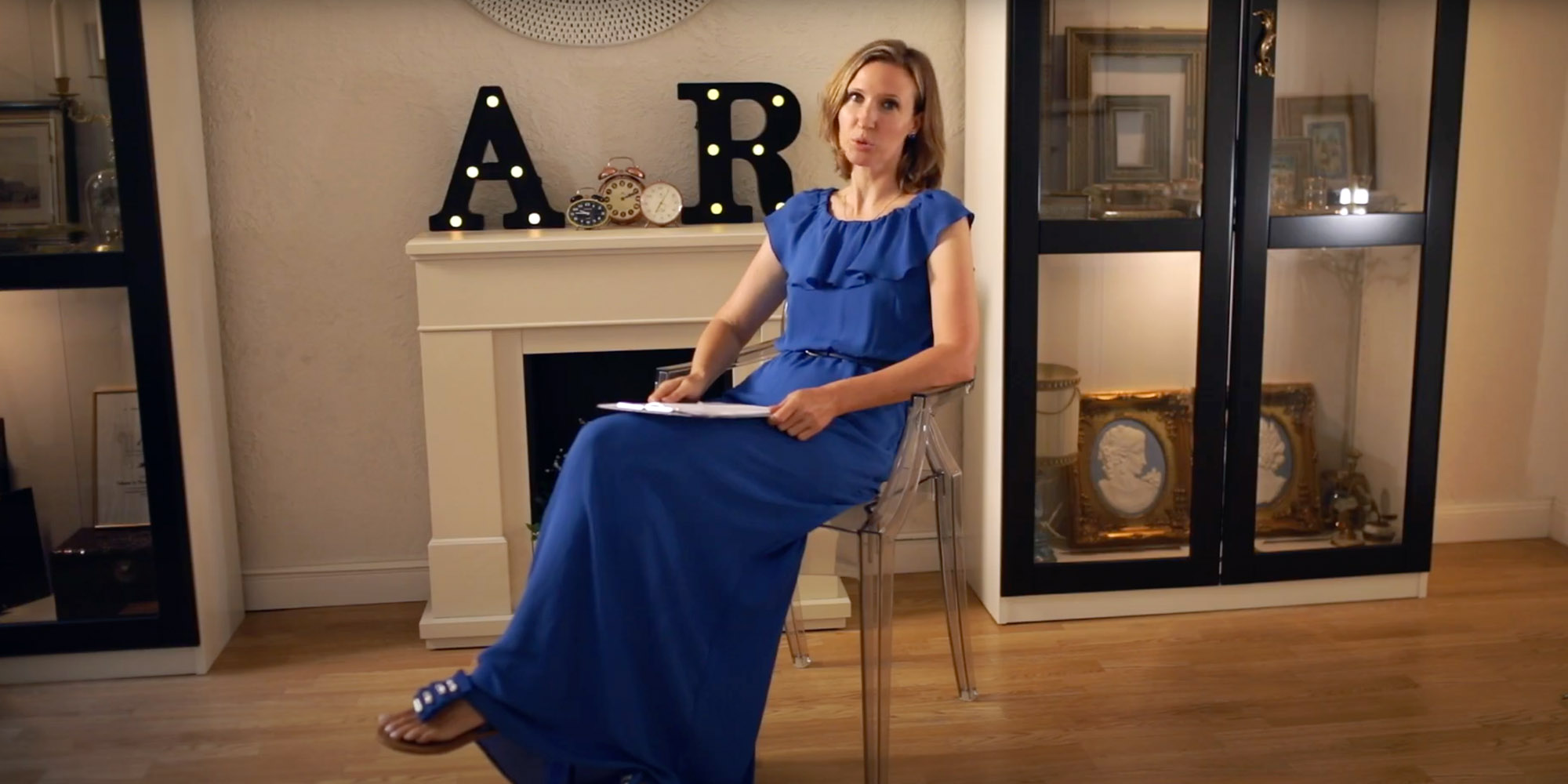 Woman in blue dress sitting next to a fireplace